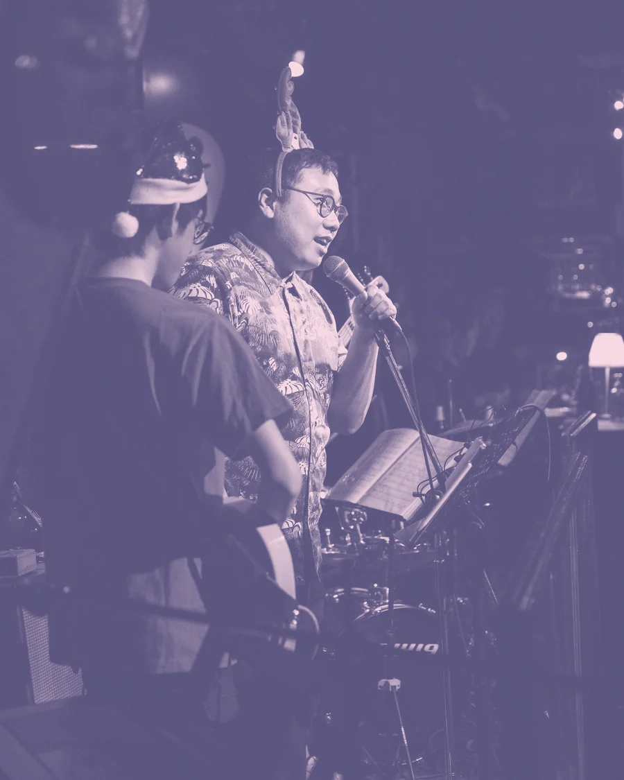 Jayson U 著住花恤衫喺台上對住 mic 唱歌，隊 band 喺側邊，risograph 粉紅藍雙色印刷